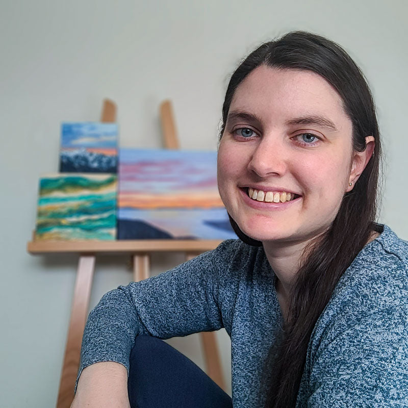 Headshot of Amanda Wondergem with a few paintings on an easel behind her